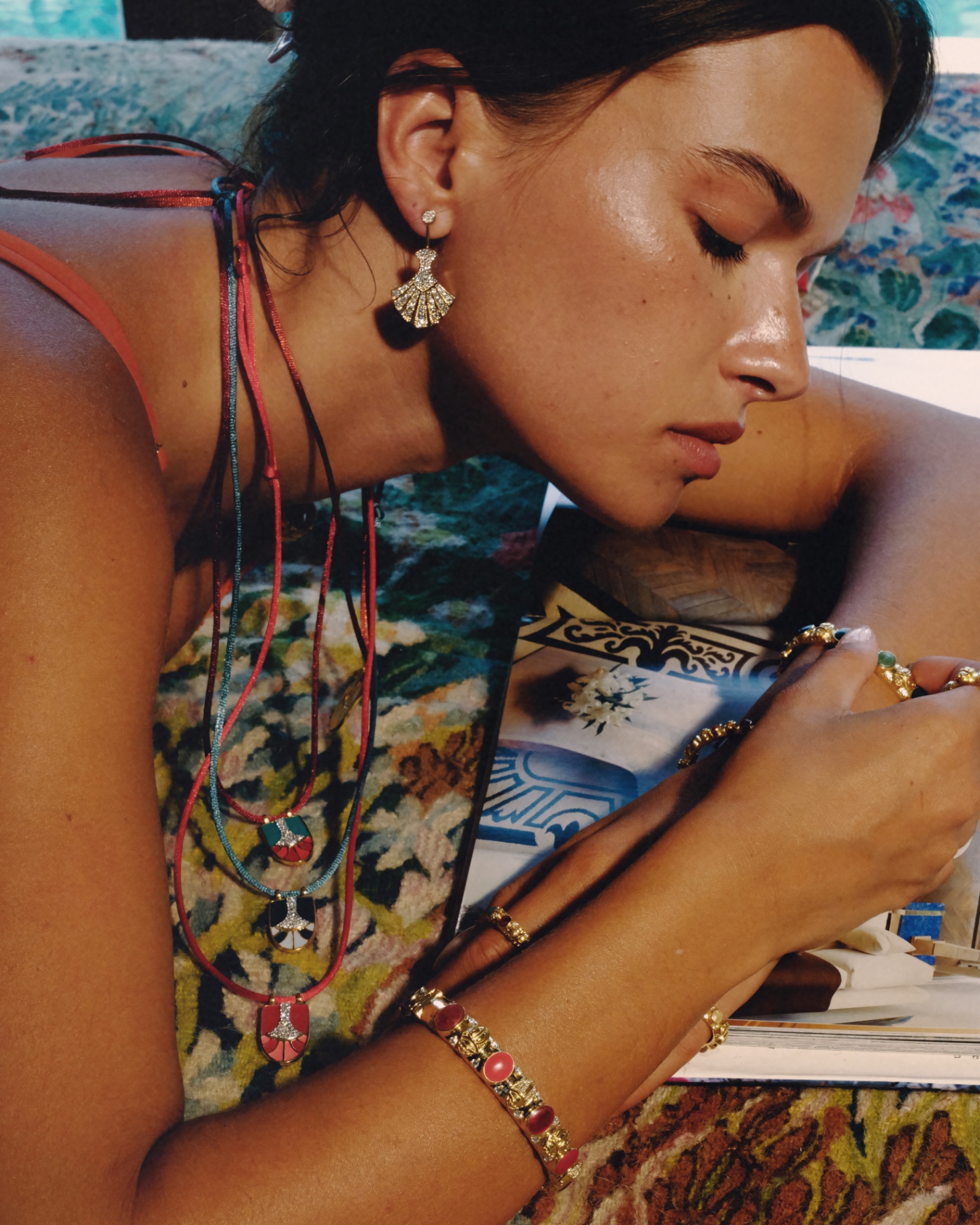 Model with a fan earring and layered necklaces leaning over an art book